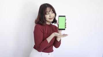 feliz punto de niña hermosa asiática en el teléfono de pantalla verde en fondo blanco foto