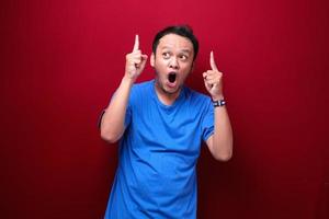 Shock Young asian man is surprised and shouting wow with pointing above with his hand isolated on red background. photo