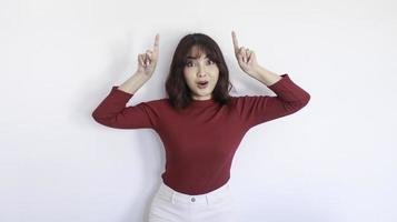 conmociona a una hermosa chica asiática apuntando arriba con una camisa roja de fondo blanco foto