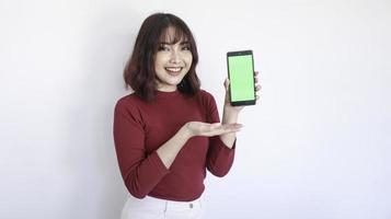 feliz punto de niña hermosa asiática en el teléfono de pantalla verde en fondo blanco foto