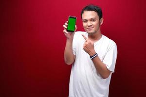 Smile Young Asian man pointing on green blank space on smartphone on red background. photo