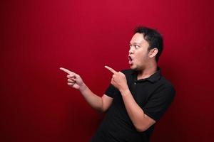 Young asian man is surprised and shouting wow with pointing right with his hand isolated on red background. photo