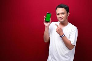 Smile Young Asian man pointing on green blank space on smartphone on red background. photo