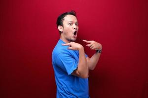 Young asian man is surprised and shouting wow with pointing right with his hand isolated on red background. photo