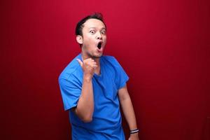 Young asian man is surprised and shouting wow with pointing right with his hand isolated on red background. photo