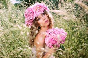 hermosa mujer caucásica con una corona de peonías rosas en la cabeza. primavera, flor, concepto de hadas foto