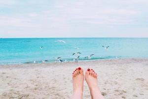 woman's feets with red nails on the sea shore background photo