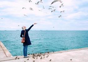 mujer rubia alimentando gaviotas en un día nublado de otoño en la costa del mar foto