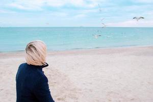blonde woman and seagulls in cloudy day on the sea coast photo