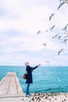 blonde woman feeding seagulls in cloudy autumn day on the sea coast photo