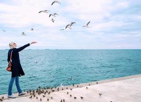 blonde woman feeding seagulls in cloudy autumn day on the sea coast photo