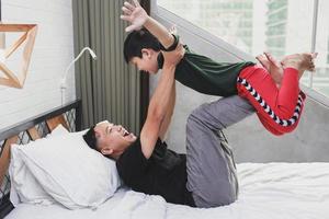 Asian young father playing with his little boy and having fun together on the bed photo