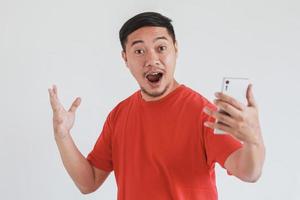 Wow face expression of Asian man wearing red t-shirt get surprised while holding smart phone photo