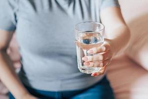 la mujer se sienta en la cama y sostiene un vaso de agua limpia en sus manos. dia Mundial del Agua. foto