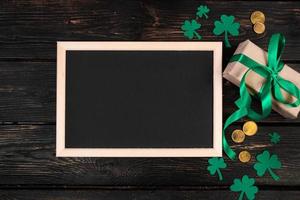 Happy St. Patrick's Day concept. Clover shamrock, gold coins and gift with green ribbon on a brown wooden background. photo