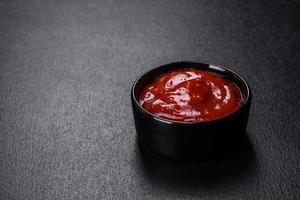 Red tomato sauce ketchup in a black ceramic saucepan photo