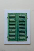 One window with closed green shutters on the background of beige wall. photo