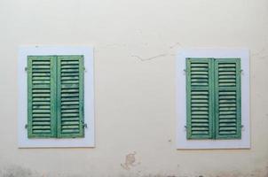 Two Windows are closed by green shutters against a beige wall. photo