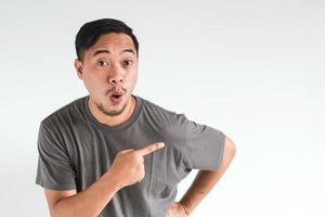 Wow and surprised face expression of Asian man in grey t-shirt with hand point on empty space photo