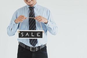 Captura de pantalla de un vendedor sonriente con camisa azul y corbata posando con un letrero de venta sobre fondo blanco. foto