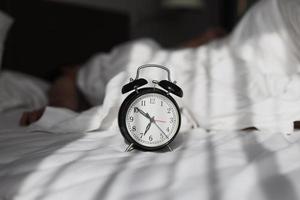 Classic alarm clock showing 7 oclock with blurry background of person sleeping on the bed photo