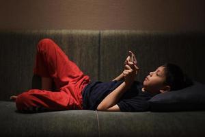 Asian boy lying on couch while playing game on smartphone before sleep photo