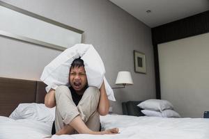 Sad asian boy covering his ears by pillow while screaming on the bed photo