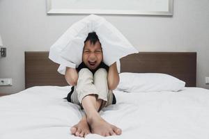 Sad asian boy covering his ears by pillow while screaming on the bed photo