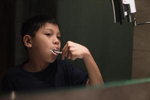 niño asiático cepillarse los dientes en el baño foto