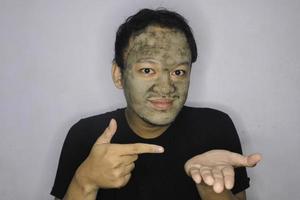 Smile Asian Man pointing in hand when he use beauty face mask photo