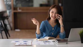 Mujer asiática de negocios con smartphone para hacer finanzas matemáticas en un escritorio de madera en la oficina, impuestos, contabilidad, concepto financiero foto