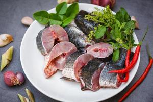 menú de pescado de cabeza de serpiente crudo fresco pescado de agua dulce, pescado de cabeza de serpiente para cocinar, pescado de cabeza de serpiente rayado picado con ingredientes hierbas y especias en plato blanco y fondo de cocina de mesa foto