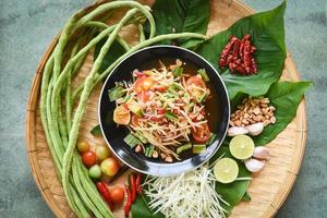 vista superior de la comida tailandesa - ensalada de papaya picante con hierbas de frijol de un metro y especias ingredientes chile tomate cacahuete ajo servido en la mesa foto