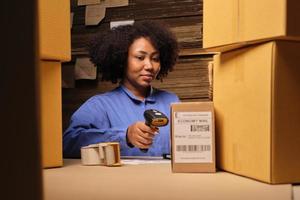 African American female worker in safety uniform using bar code scanner to check shipment orders at parcels warehouse, paper manufacture factory for the packing industry, logistic transport service. photo