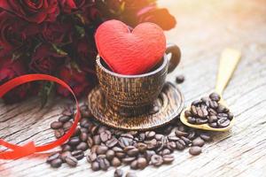 corazón en taza de café de madera con granos de café amor romántico día de san valentín y flor rosa roja sobre fondo de madera - concepto de amor café foto