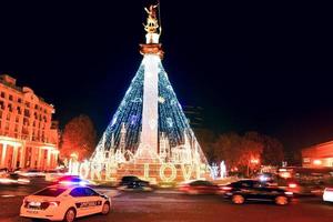 Police patrol vehicle stand in street on roundabout and passing cars on roundabout pass in freedom square on Christmas holidays. Xmas celebrations in caucasus photo