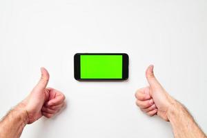 la mano de la mujer muestra un teléfono inteligente móvil con pantalla verde en posición vertical aislado en un fondo verde con el pulgar hacia arriba. maqueta del espacio en blanco de la pantalla móvil foto