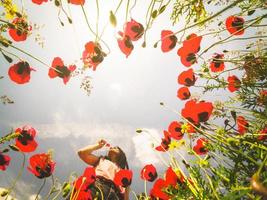 Caucasian young woman hold poppy flower close to face in summer field happy outdoors. Concept freedom and summer joy in nature. photo