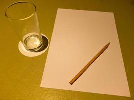 On the table are a glass of A4 paper water and brown wooden pencils. photo