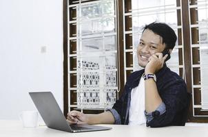 Young Asian man happy and smile what he see in the laptop when in call on smartphone photo