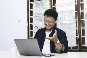 Young Asian man happy and excited when video call with laptop on table. photo