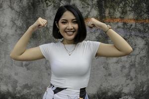 Gorgeous strong young asian woman with whute shirt showing biceps and smiling. Indonesian girl strong concept. photo