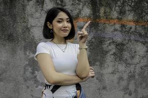 gesto de pensamiento de una hermosa chica asiática apuntando al lado con camisa blanca. foto