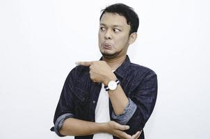 Angry and hate face of young Asian man in shirt with hand point on empty space. photo