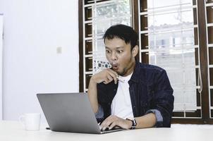 Young Asian man shocked and wow what he see in the laptop. photo