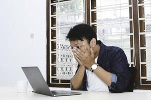 un joven asiático que se siente estresado y confundido cuando trabaja con una laptop en la mesa. foto