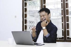 Young Asian man happy and excited when video call with laptop on table. photo