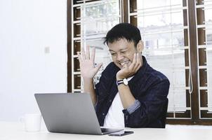 Young Asian man happy and excited when video call with laptop on table. photo