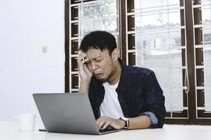 Young Asian man feeling stress and sad when work laptop on table. photo