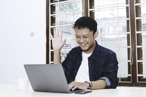 Young Asian man happy and excited when video call with laptop on table. photo